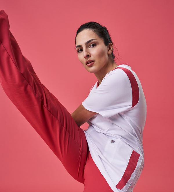 A carer is wearing a red and white outfit and holds one leg outstretched in the air.